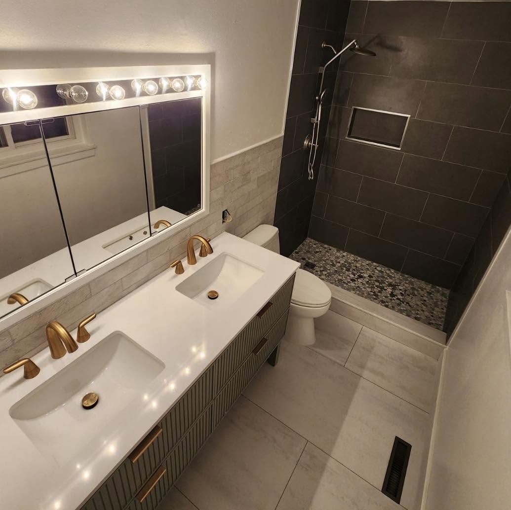 Completed bathroom remodel with floating double vanity, brushed brass faucets, quartz countertop and dark tiled walk-in shower