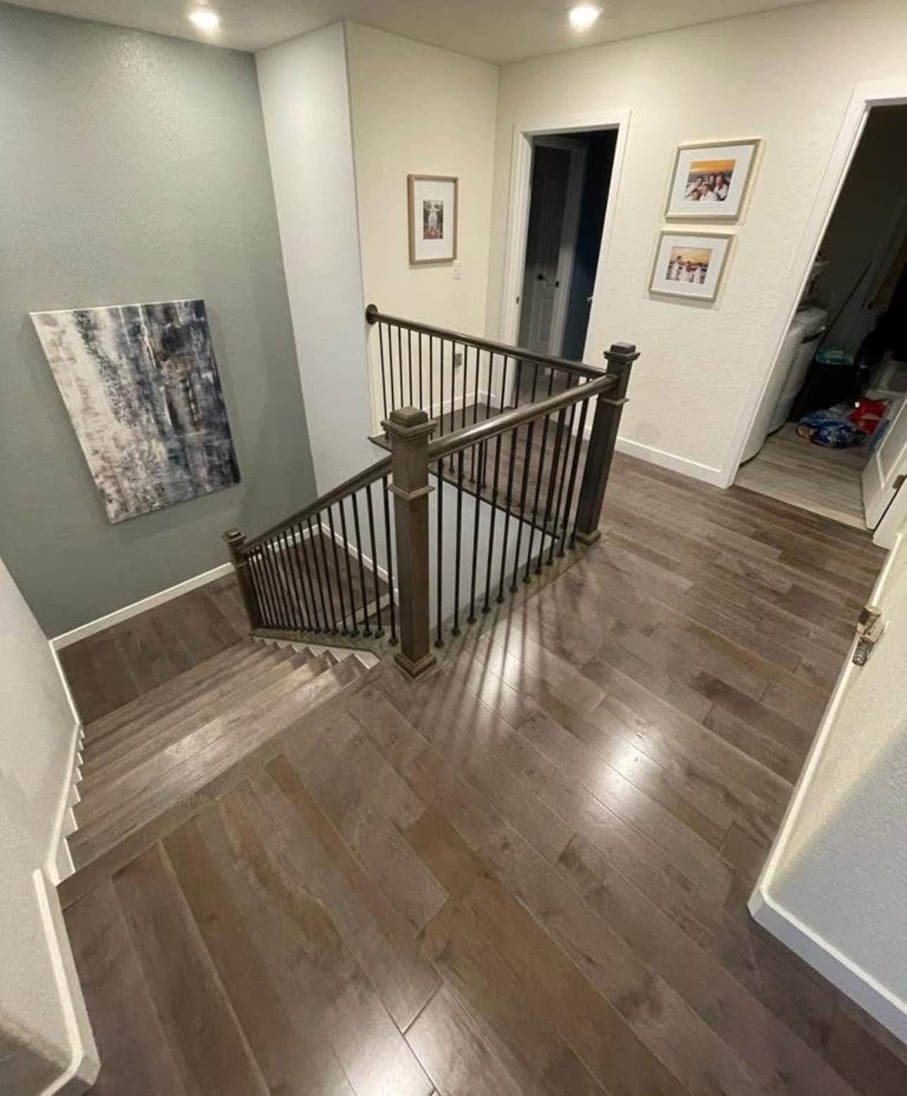 New hardwood flooring installed on an upper landing and staircase with iron balusters