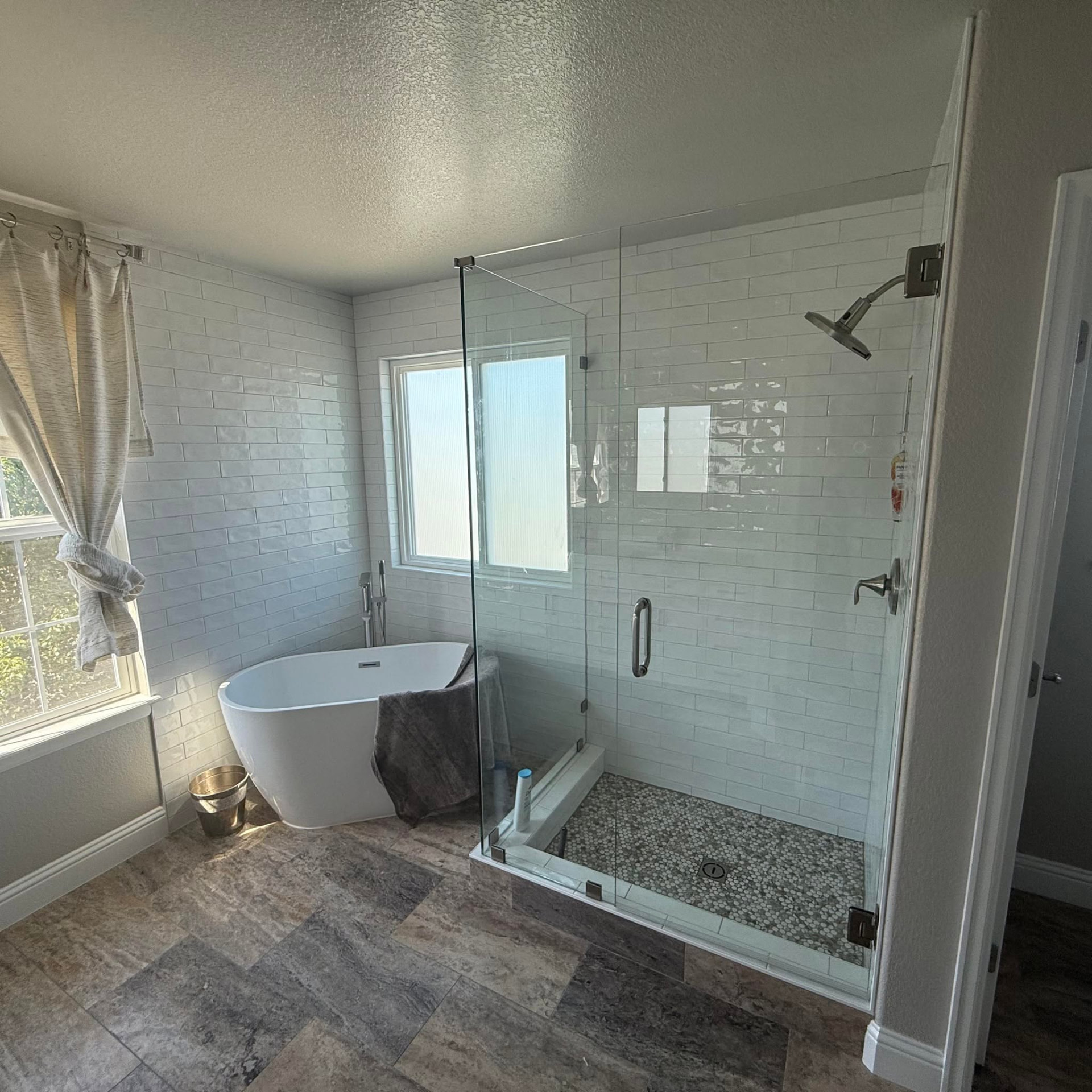 Completed primary bathroom with freestanding soaking tub, frameless glass shower and white subway tile