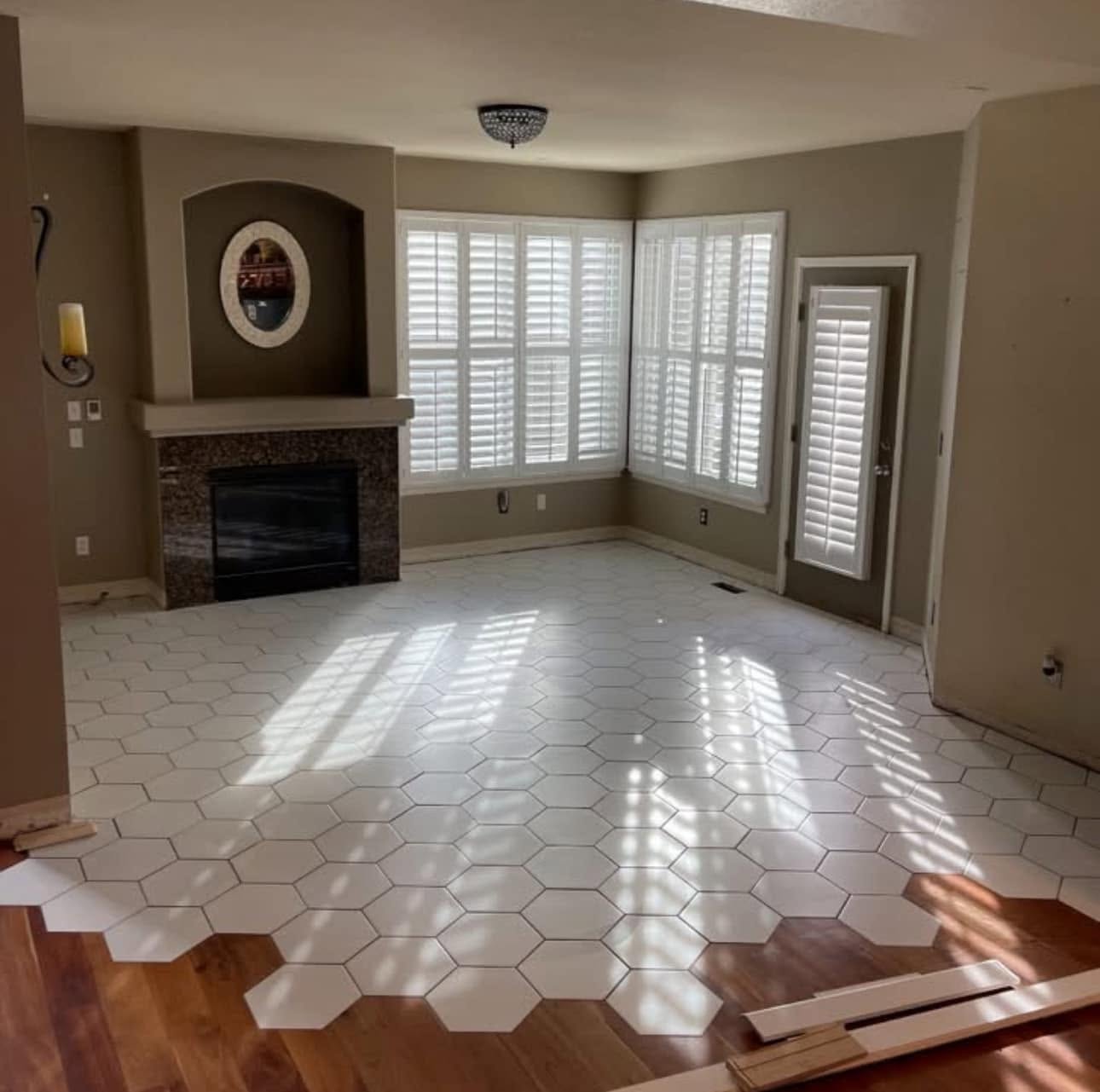 White hexagon tile floor installation transitioning into hardwood flooring in a living room with fireplace