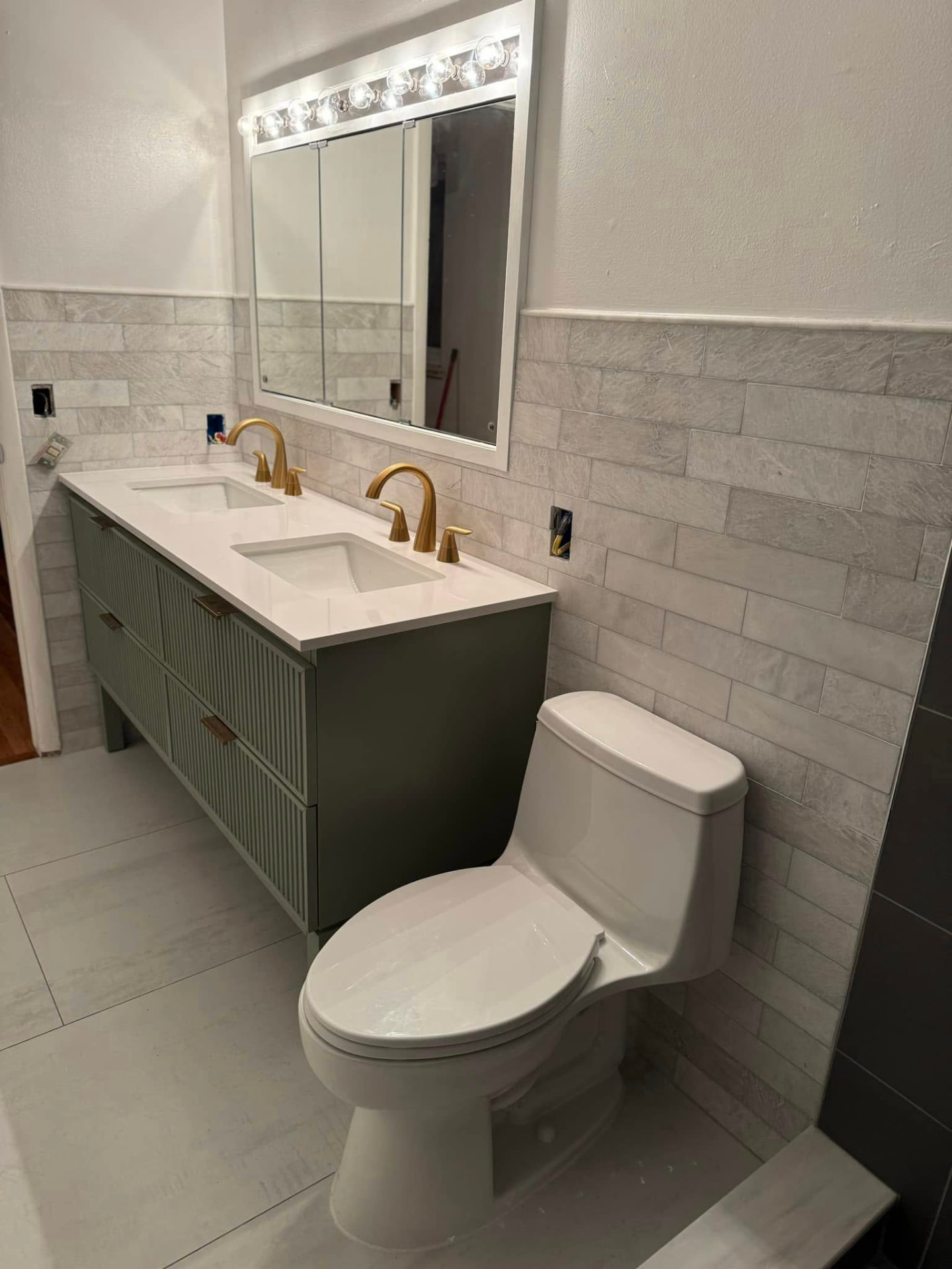 Remodeled bathroom with double vanity, brass fixtures, stone-look wall tile and new toilet